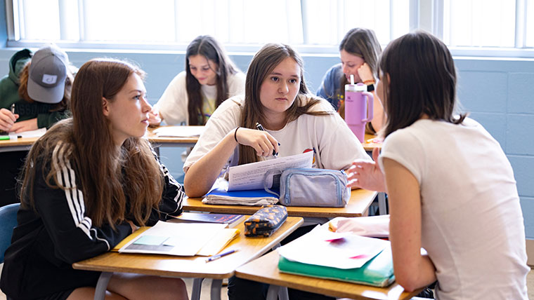 Three students adjoin their desks to discuss their classwork together.